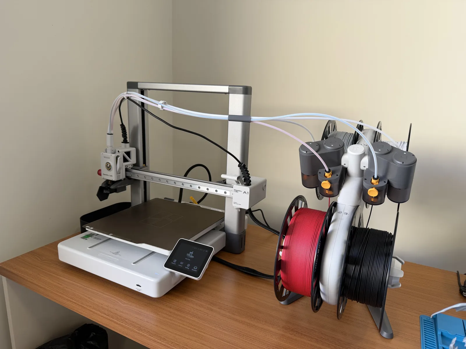 Impressora 3D Bambu Lab A1 no laboratório da Abrahao Labs com sistema AMS de 4 filamentos ao lado, sobre bancada de madeira